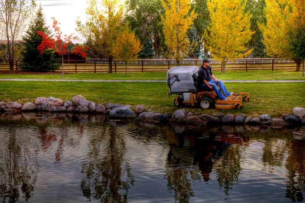 landscaper mowing grass near pond