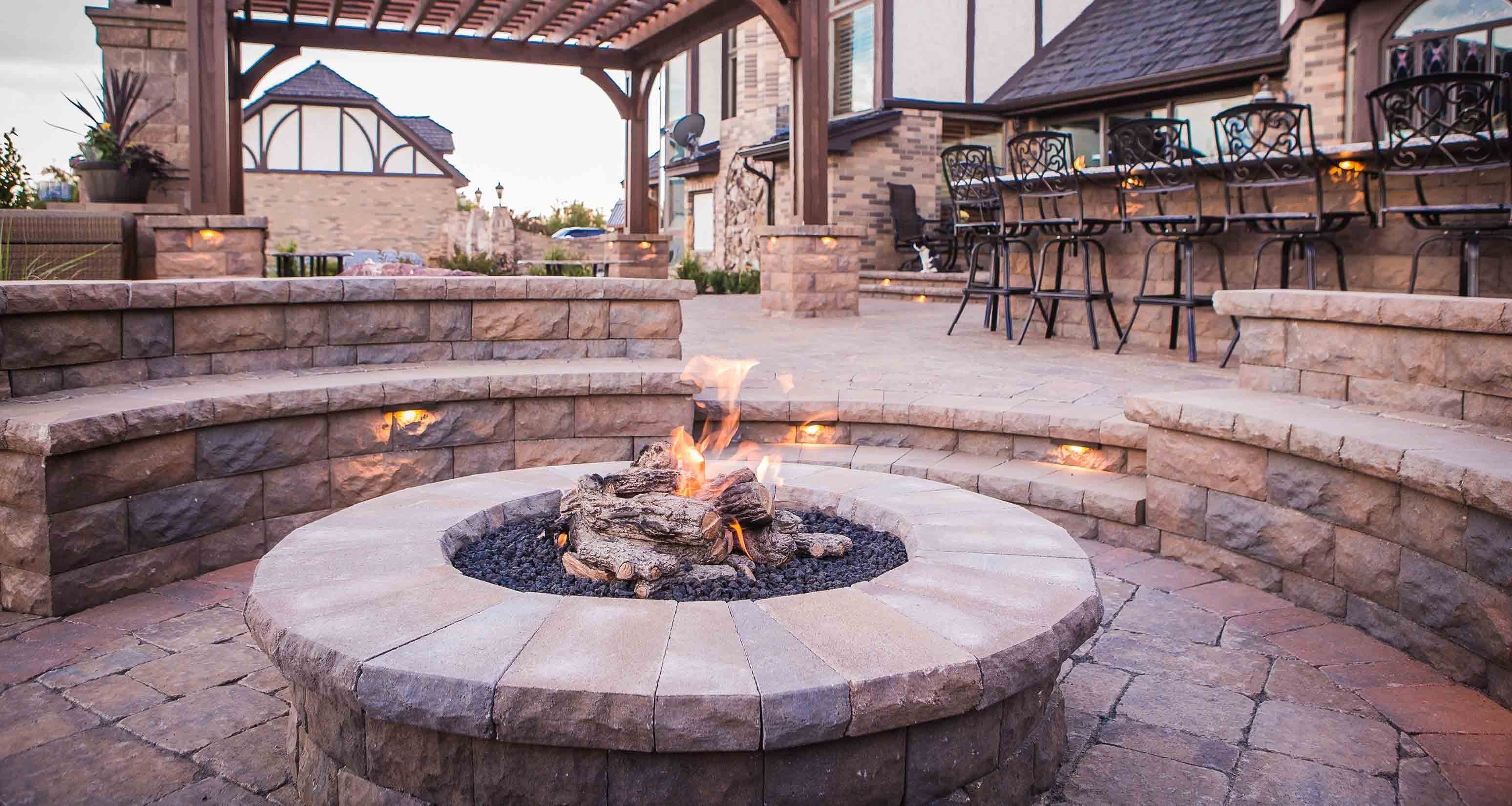 firepit near outdoor kitchen with built in seating and lighting