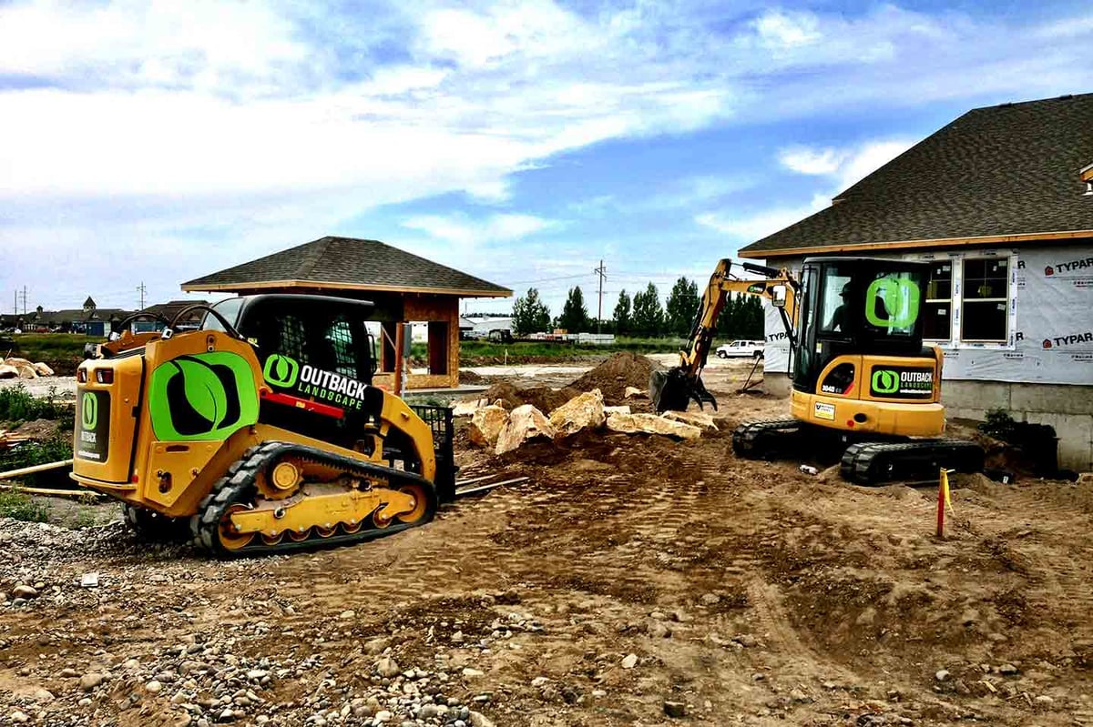 skid loader and front loader move landscape rocks